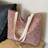 A pink bohemian corduroy tote bag with light beige straps resting on a cardboard box.