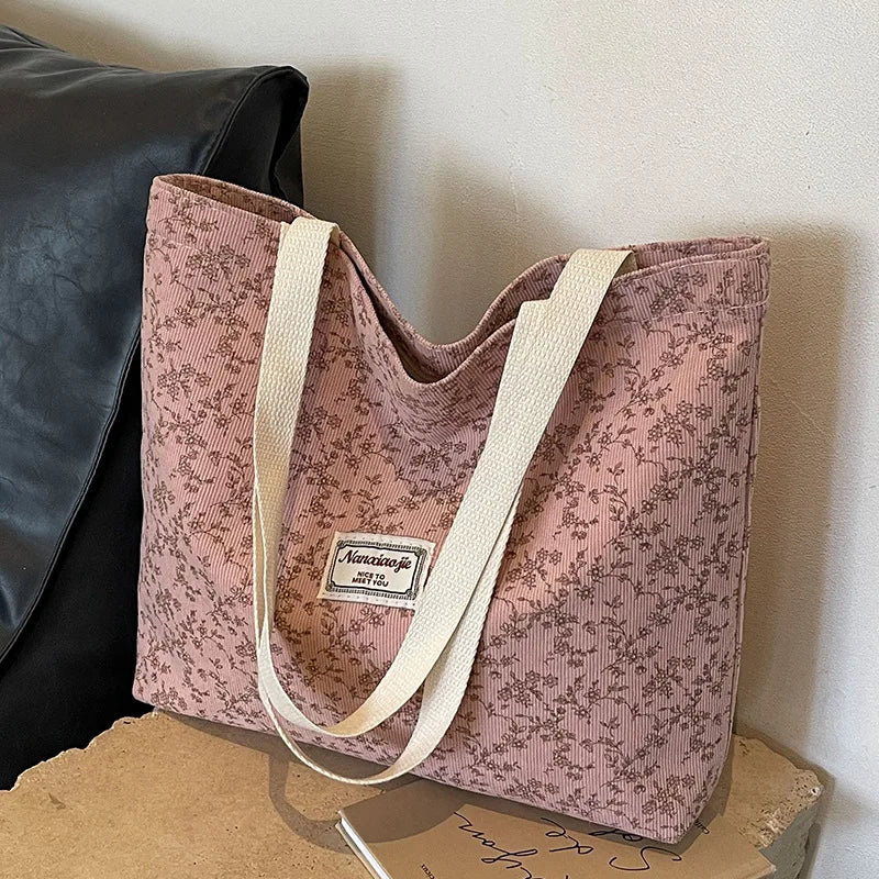 A pink bohemian corduroy tote bag with light beige straps resting on a cardboard box.