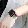 A wrist wearing a colorful braided stretch band on the wrist alongside an Apple Watch.