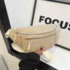 A beige corduroy crossbody waist bag with a silver zipper and adjustable strap is held by a hand against a white background.