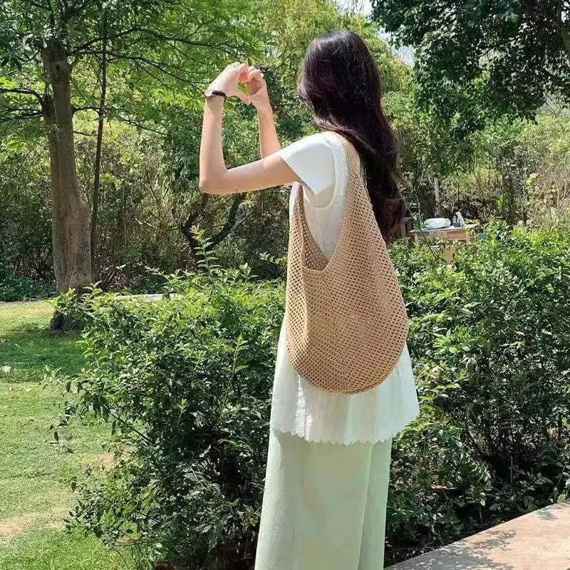 A woman stands outdoors holding a beige crochet shoulder bag with mesh detailing.