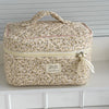A beige floral print quilted cosmetic bag with a light yellow zipper and fabric ribbon.