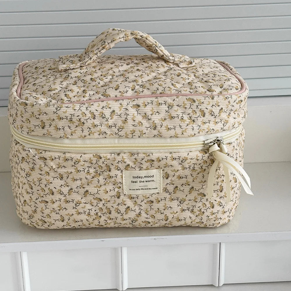 A beige floral print quilted cosmetic bag with a light yellow zipper and fabric ribbon.