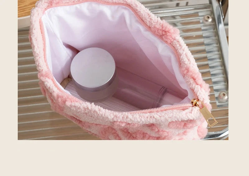A pink plush storage bag lined with pink fabric holds a round cosmetic container on a metal tray.