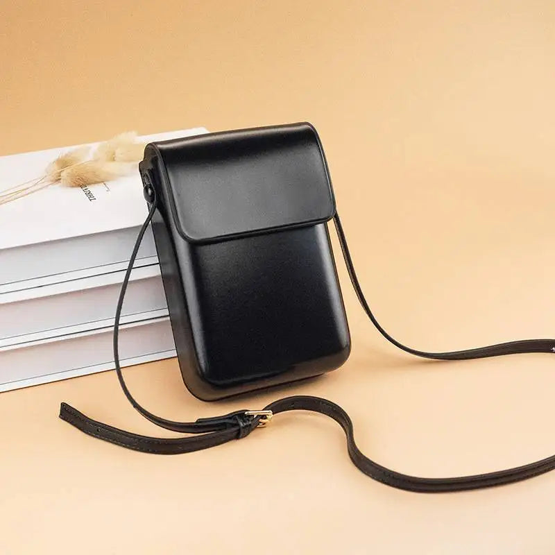 A black vintage PU leather crossbody bag with an adjustable strap resting on a light beige surface.