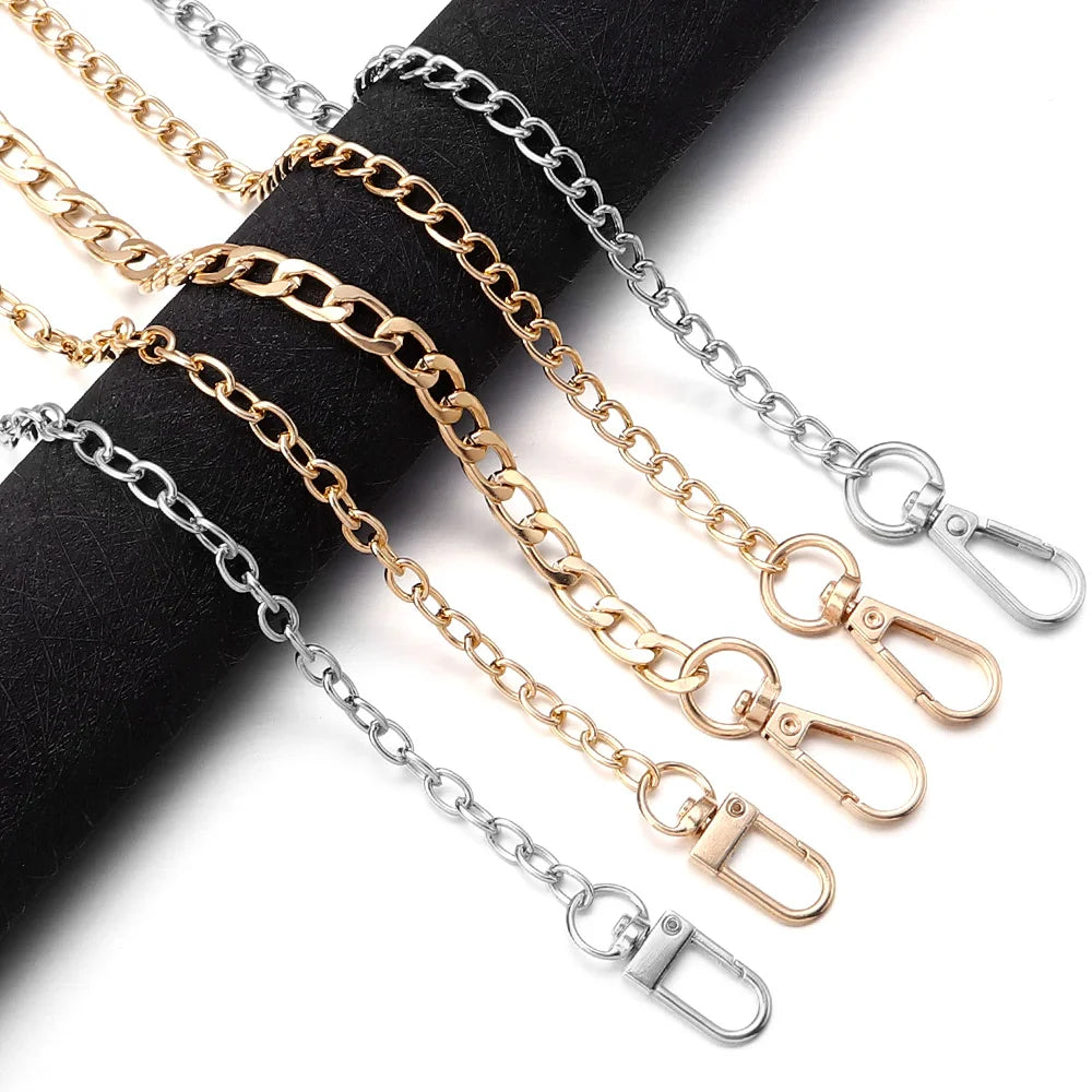 A collection of adjustable metal bag strap chains in gold and silver tones laid out on a black surface.