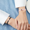 A close-up of two wrists wearing beaded friendship bracelets, one pink and one black, against a blue fabric background.