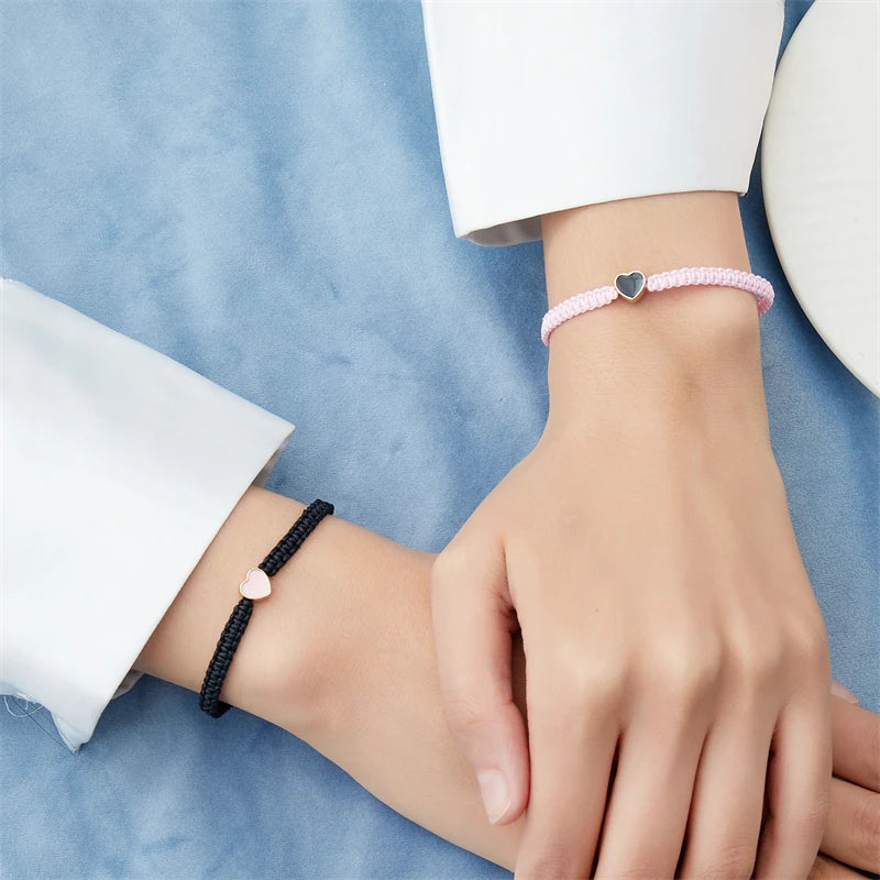 A close-up of two wrists wearing beaded friendship bracelets, one pink and one black, against a blue fabric background.