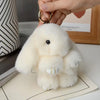 A fluffy white plush rabbit charm hanging from a gold-colored keyring.