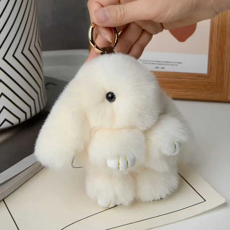 A fluffy white plush rabbit charm hanging from a gold-colored keyring.
