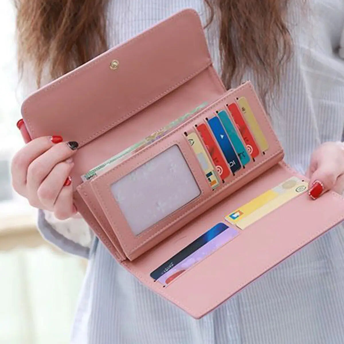 A pink quilted long wallet with a crown buckle is shown being held by a person.