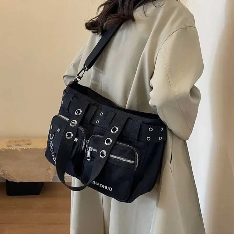 A black nylon shoulder bag with metal rivets and a strap is worn by a person in a light colored coat.