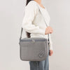 A woman is holding a gray insulated lunch tote bag with a strap against a light background.