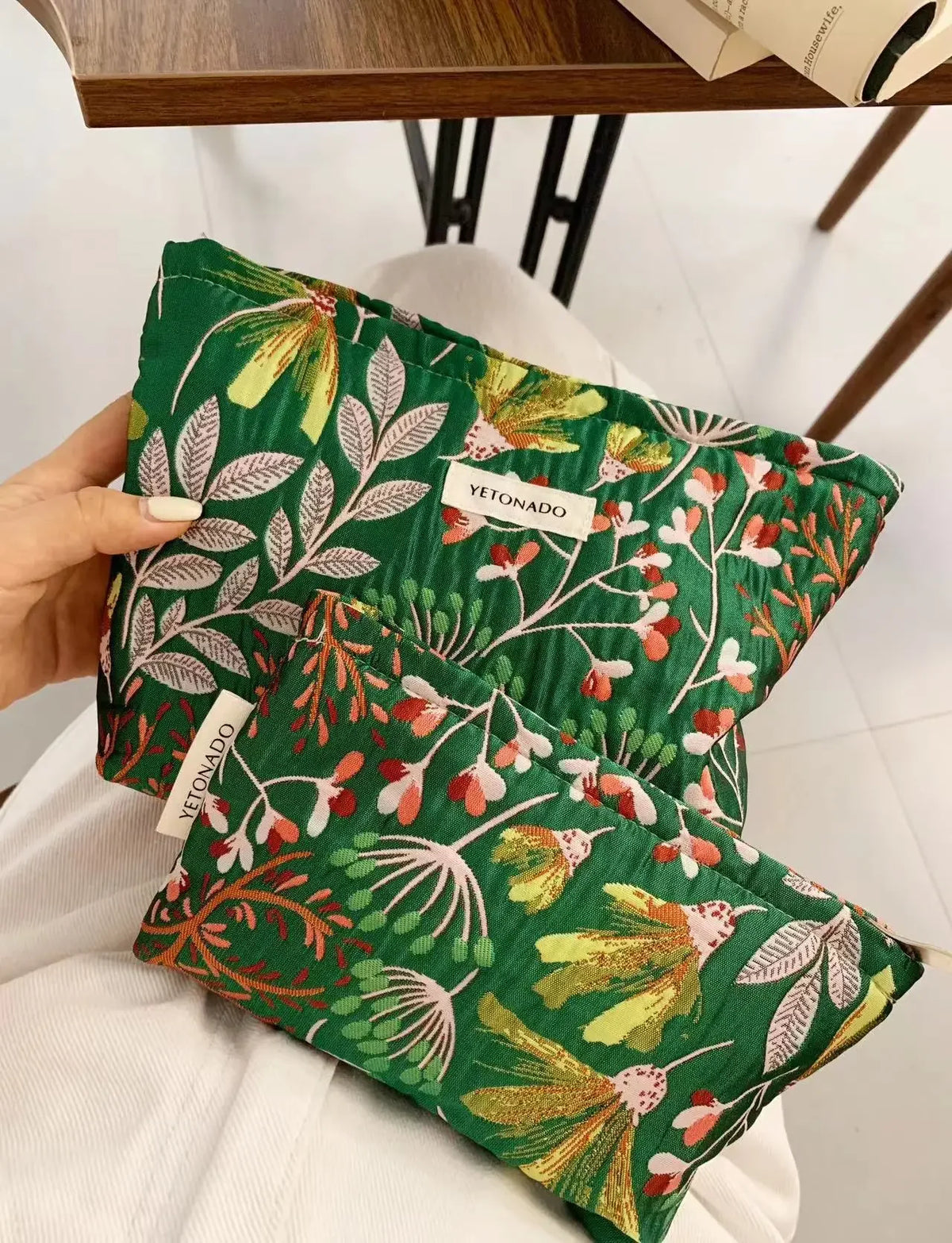 A green fabric pouch with a botanical print featuring leaves and small flowers is held by a hand.
