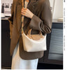 A woman wearing a brown blazer and white dress holds a beige leather crossbody handbag.