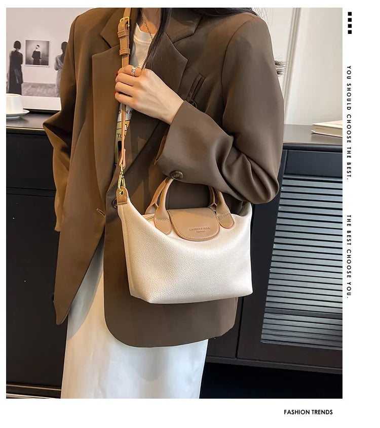 A woman wearing a brown blazer and white dress holds a beige leather crossbody handbag.