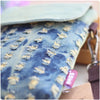 A close-up of a denim mini messenger bag with light blue fabric and yellow stitching, showing the texture and detail.