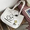 A white canvas shoulder bag featuring a Snoopy cartoon design, resting on a woven mat.