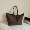 A brown leopard print canvas tote bag with handles resting on a white surface next to a notebook.