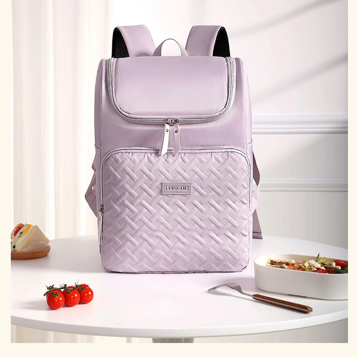 A light purple insulated travel backpack with black straps and a quilted pattern sitting on a white table.