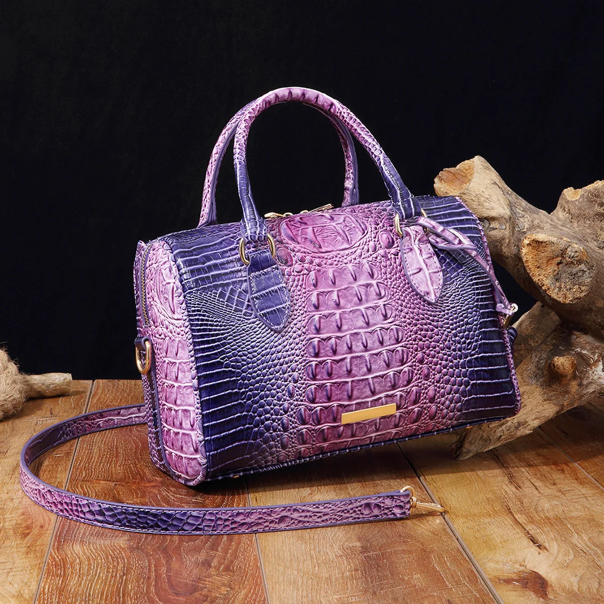 A purple and blue crocodile pattern luxury handbag resting on a wooden surface next to a piece of driftwood.