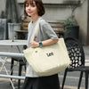 A woman wearing a grey t-shirt and black shorts holds a cream colored Lee Oxford cloth tote bag.