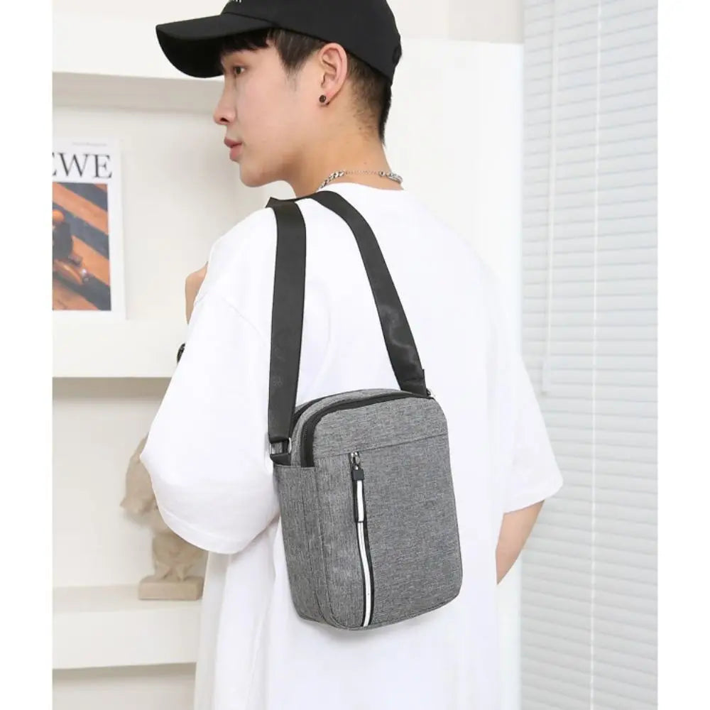 A man wearing a white shirt and black hat holds a gray durable waterproof crossbody bag.