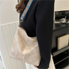 A beige leather shoulder bag with a blue embroidered strap is shown hanging from a black blazer sleeve.