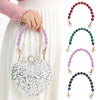 A silver heart-shaped bag chain made of sparkling stones is displayed against a white skirt.