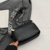 A hand holds a black vegan PU crossbody bag with a patterned strap and a gray blazer.