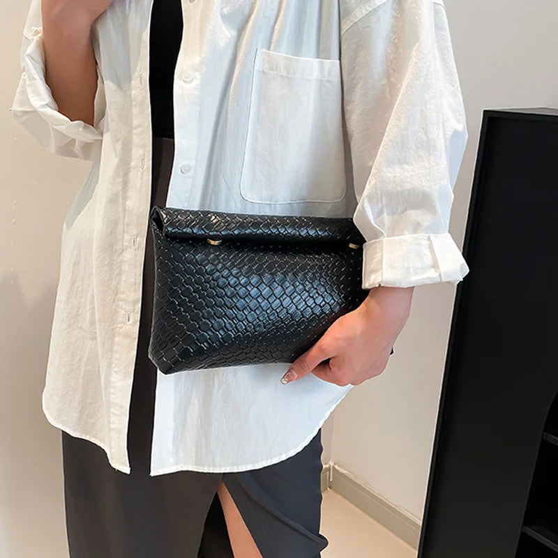 Una mujer sostiene un bolso de mano tejido negro con textura de cocodrilo bajo una camisa blanca.