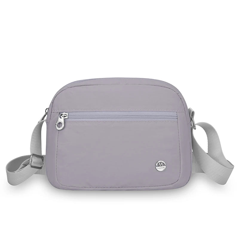 Helles lila Nylon-Crossbody-Tasche mit Klappverschluss und verstellbarem Riemchen vor weißem Hintergrund