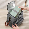 A hand is opening a gray insulated lunch bag to reveal a light green insulated food container.