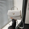 A white quilted shoulder messenger bag with a silver hardware is held by a person in front of a window blind.