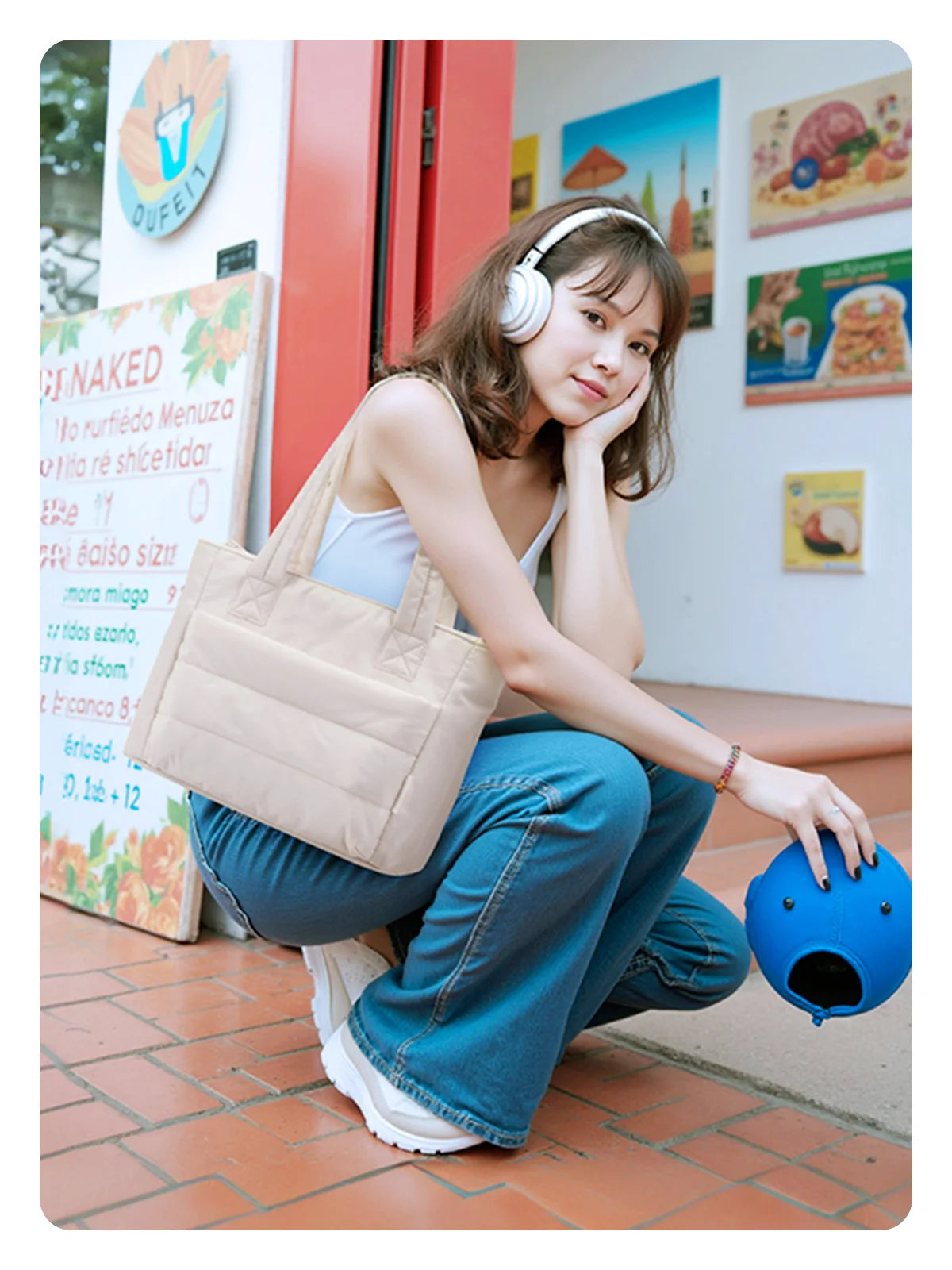 Une jeune femme en haut blanc et jean bleu, assise au sol tenant un sac à puces beige matelassé.
