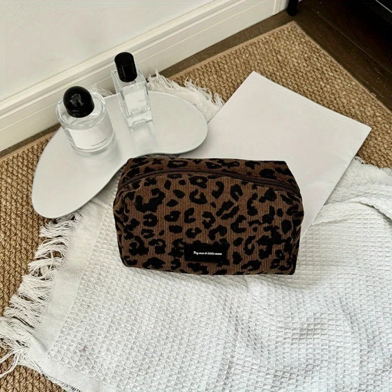 A leopard print makeup organizer bag resting on a white towel next to glass bottles.