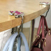 A set of pink and gold portable cat handbag hooks are displayed on a wooden table surface.