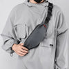 A person wearing a gray hoodie is holding a black water-resistant nylon waist bag with an adjustable strap.