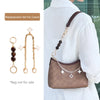 A gold chain with decorative charms is shown next to a brown leather handbag being worn on a white shirt.