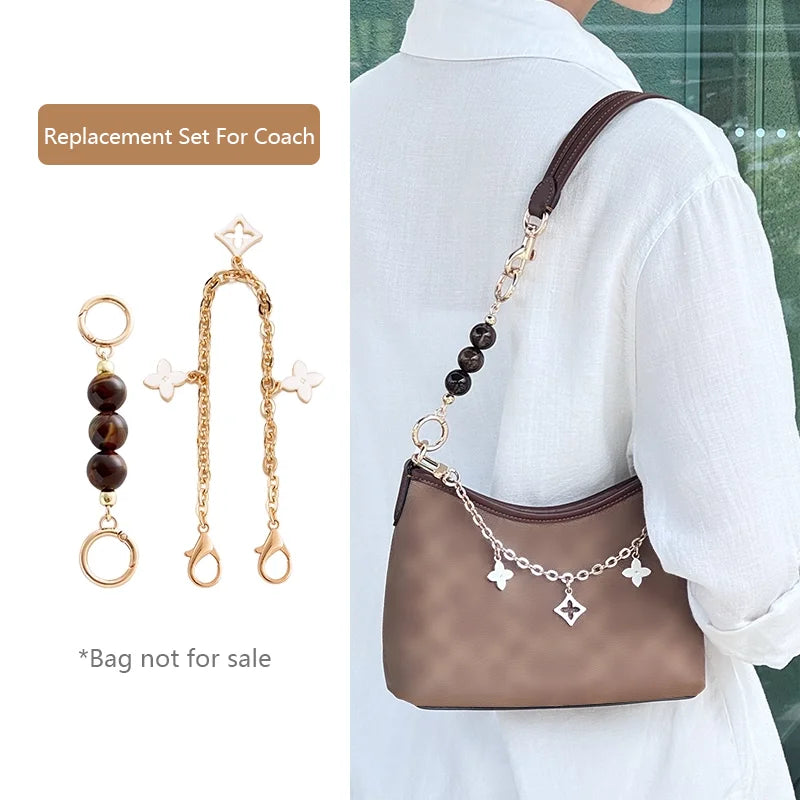 A gold chain with decorative charms is shown next to a brown leather handbag being worn on a white shirt.