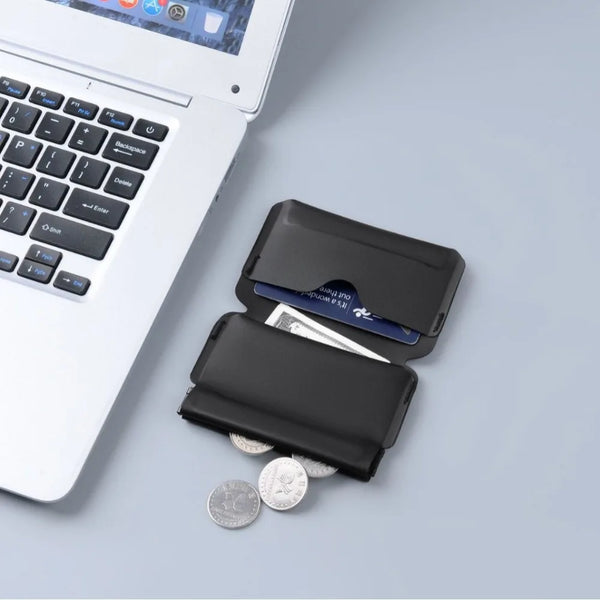A black magnetic foldable ID card holder and coin purse resting on a light gray surface next to a laptop.