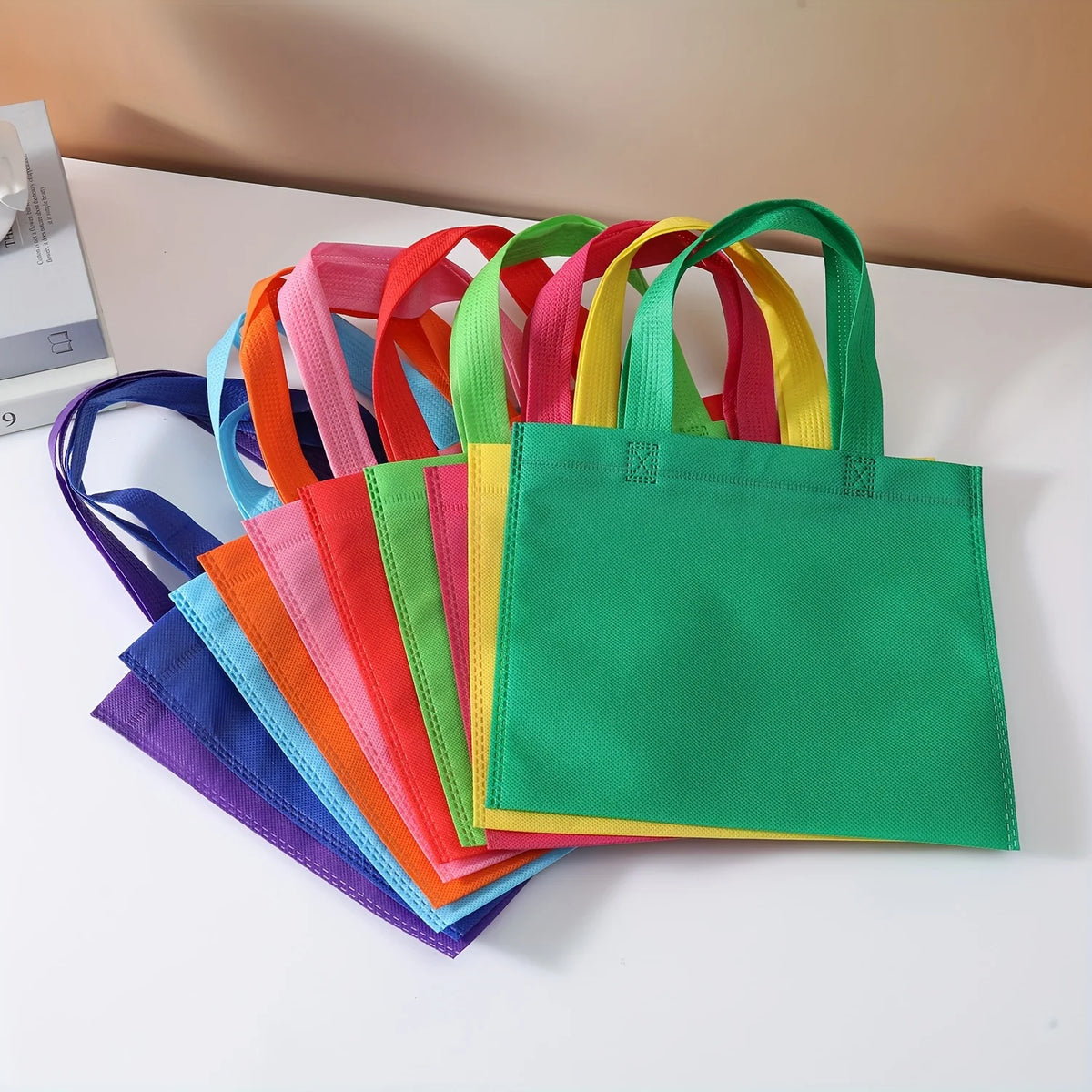 A colorful stack of non-woven tote bags in various shades of pink, orange, yellow, and green.