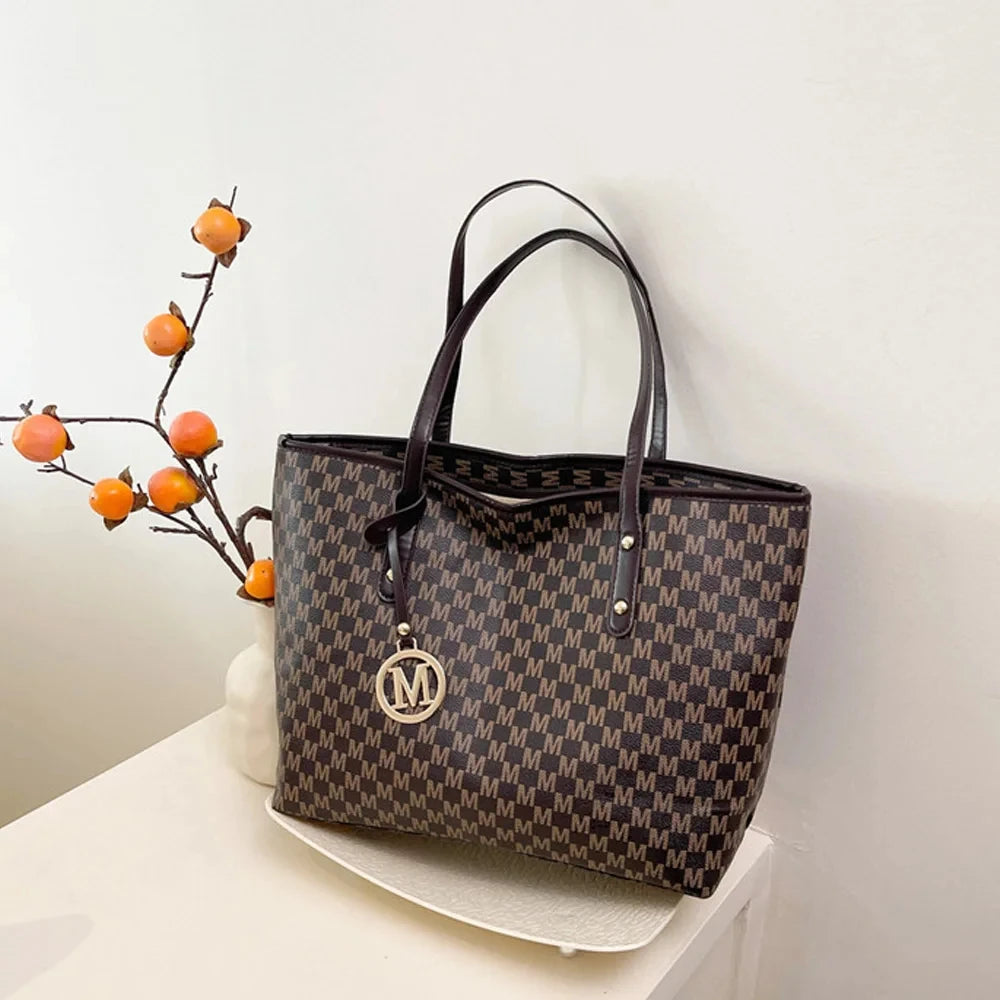 A dark brown faux leather tote bag with a monogram print is displayed against a white wall.