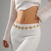 A close-up of a woman wearing a white knitted top and pants, accessorized with a vintage gold plated sunflower smiley face wa