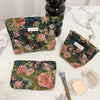 A floral patterned velvet cosmetic pouch in deep green and pink is displayed on a white marble surface.