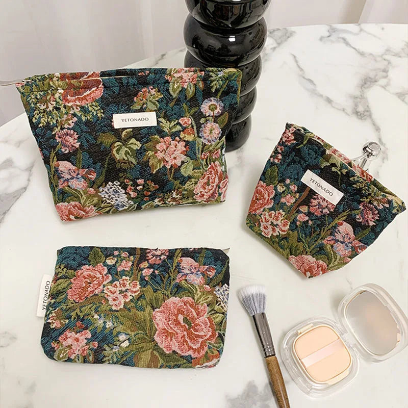 A floral patterned velvet cosmetic pouch in deep green and pink is displayed on a white marble surface.