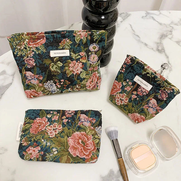 Pochette cosmétique en velours à motif floral vert foncé et rose sur une surface en marbre blanc.
