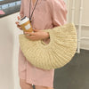 A person holds a beige woven rattan half-moon beach handbag against a light pink dress.