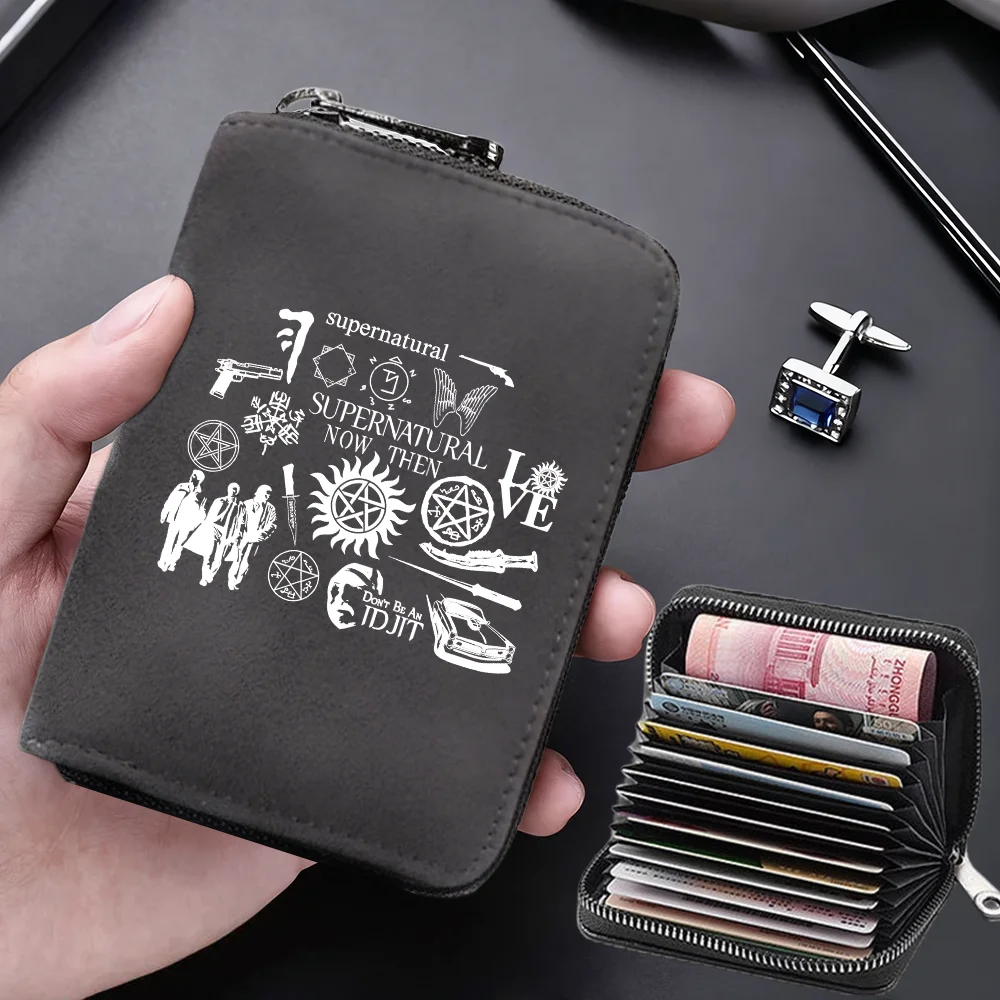 A dark gray compact card wallet with a leather-like finish is shown being held, featuring a supernatural design and an attach
