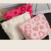 Three plush heart-pattern storage bags in pink, white, and bright pink are displayed on a dark surface.